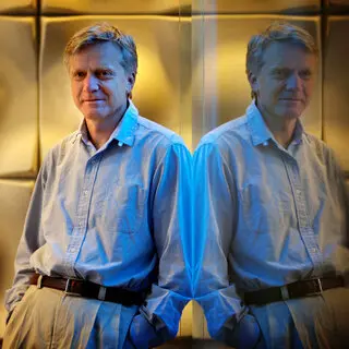 Andreas Bechtolsheim, in a button-down dress shirt and slacks, is leaning against a mirrored wall.