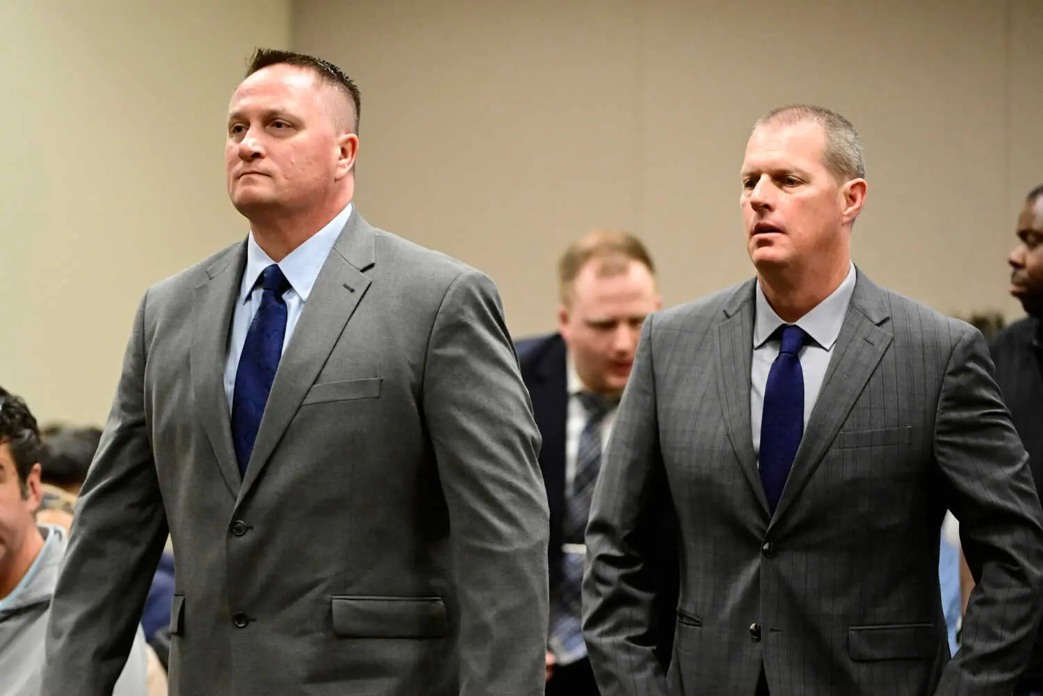 Two men in gray suits and blue ties walk in a courtroom.