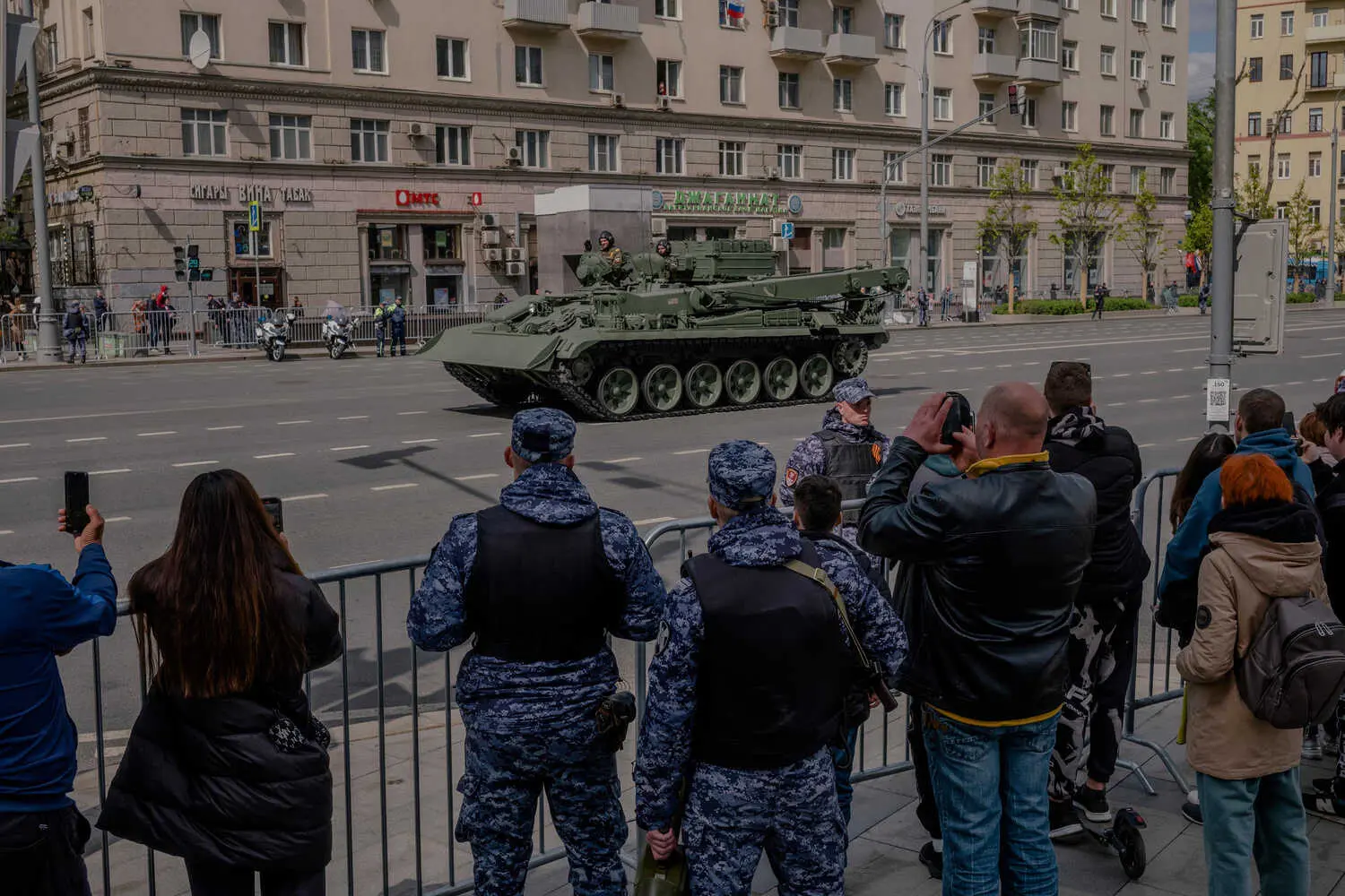 A view of people watching a military vehicle roll down a broad avenue.